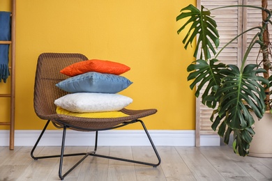 Photo of Armchair with different pillows near color wall in room