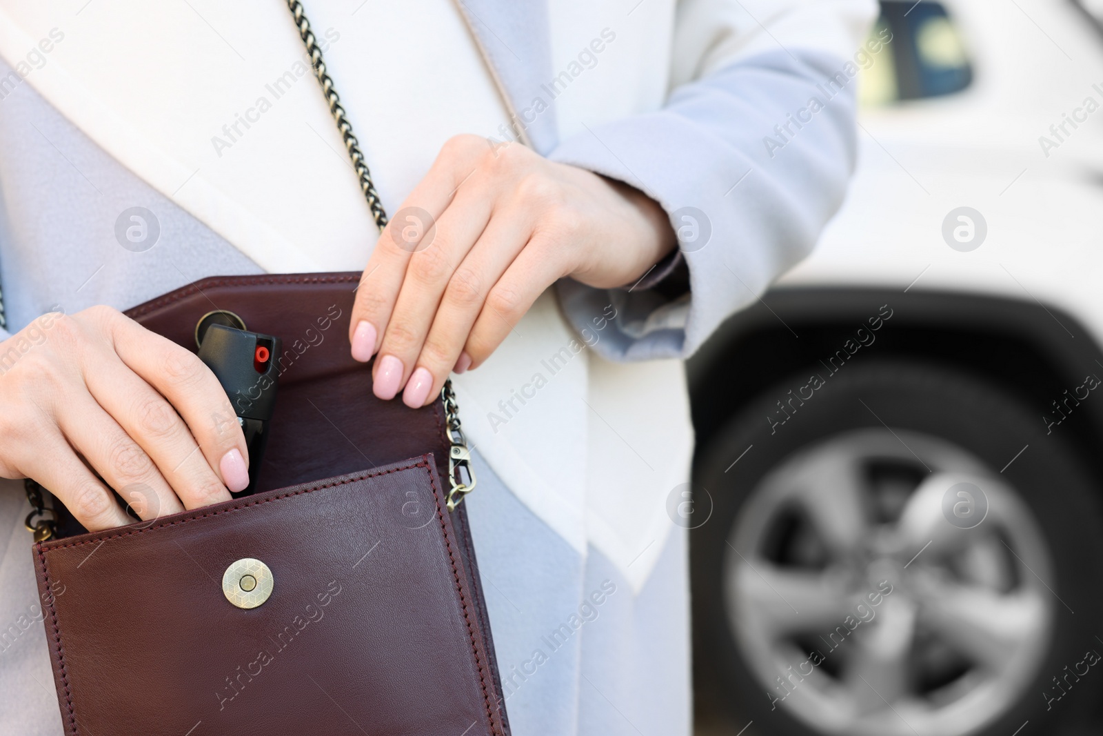 Photo of Young woman putting pepper spray into bag outdoors, closeup