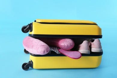 Photo of Yellow suitcase and travel pillow on light blue background