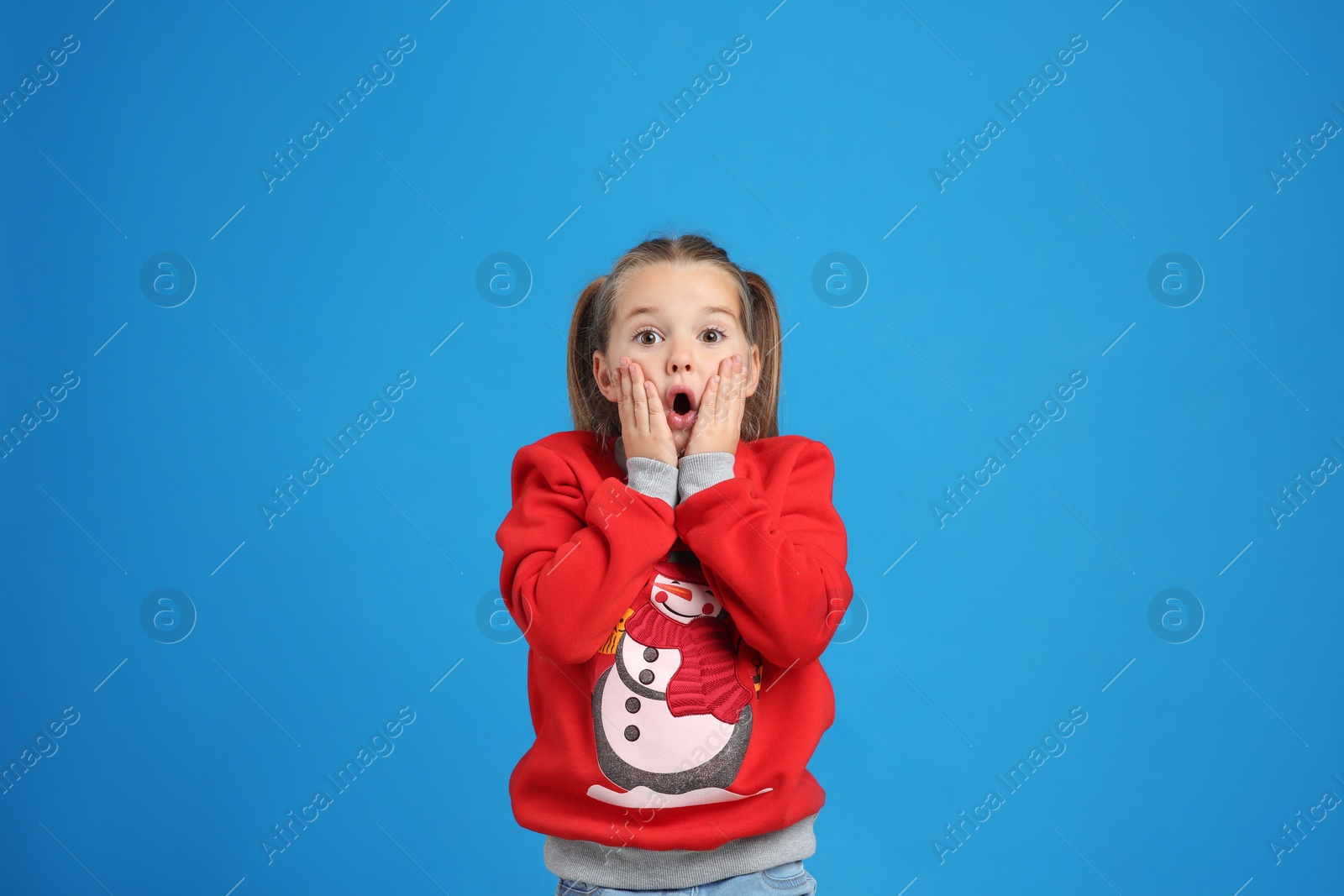 Photo of Surprised little girl in Christmas sweater on blue background
