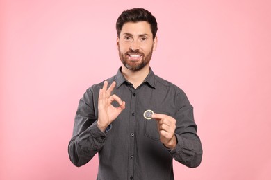 Happy man with condom showing ok gesture on pink background. Safe sex