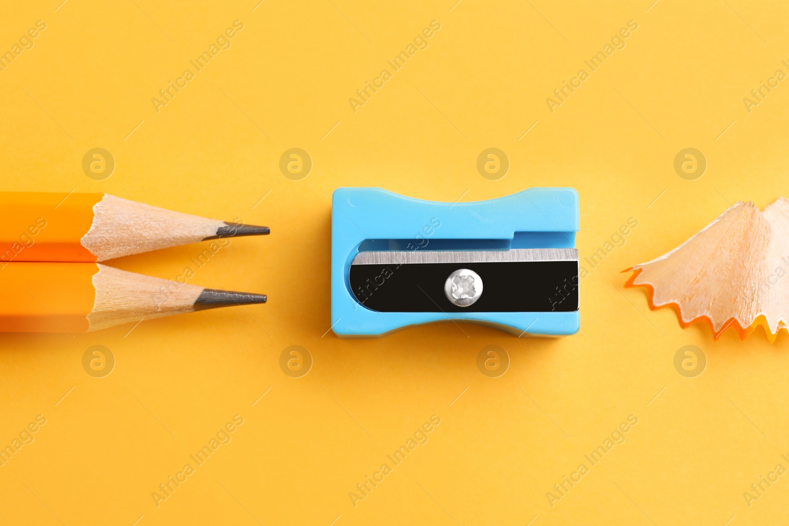 Photo of Pencils, sharpener and shavings on yellow background, flat lay