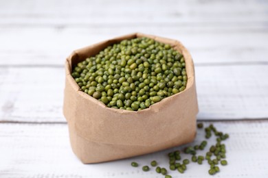 Photo of Paper bag with green mung beans on white wooden table, closeup