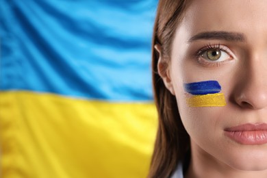Young woman with face paint near Ukrainian flag, closeup. Space for text