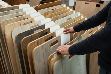 Photo of Man choosing wooden flooring among different samples in shop, closeup