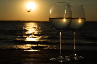 Photo of Glasses of delicious wine near sea at sunset