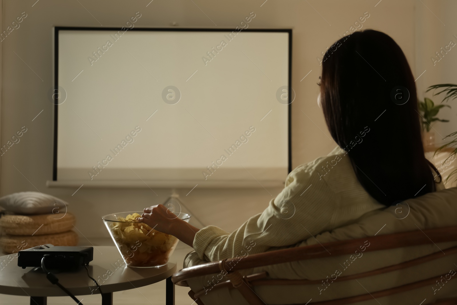 Photo of Young woman watching movie using video projector at home