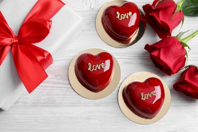 Photo of St. Valentine's Day. Delicious heart shaped cakes, roses and gift on white wooden table, flat lay