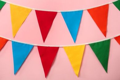 Photo of Buntings with colorful triangular flags on pink background. Festive decor