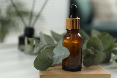 Aromatherapy. Bottle of essential oil and eucalyptus leaves on white table