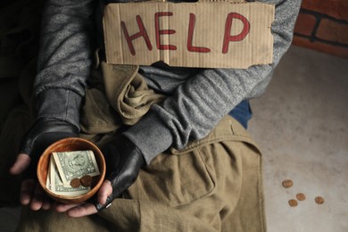 Photo of Poor homeless man with help sign holding bowl of donations on floor, above view