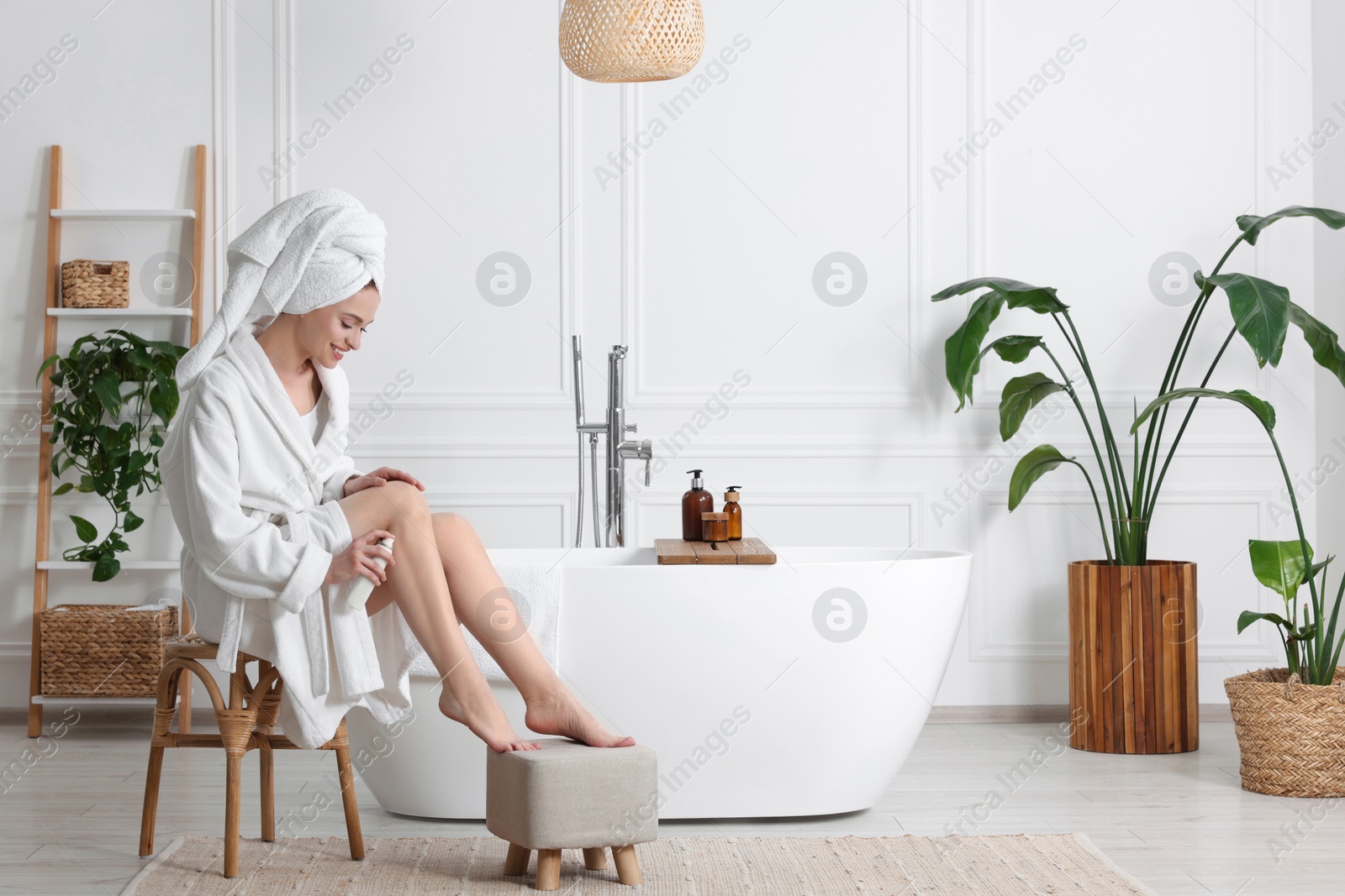 Photo of Beautiful young woman applying body spray onto legs in bathroom, space for text