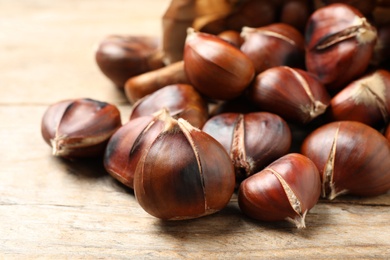 Photo of Delicious roasted edible chestnuts on wooden table, closeup
