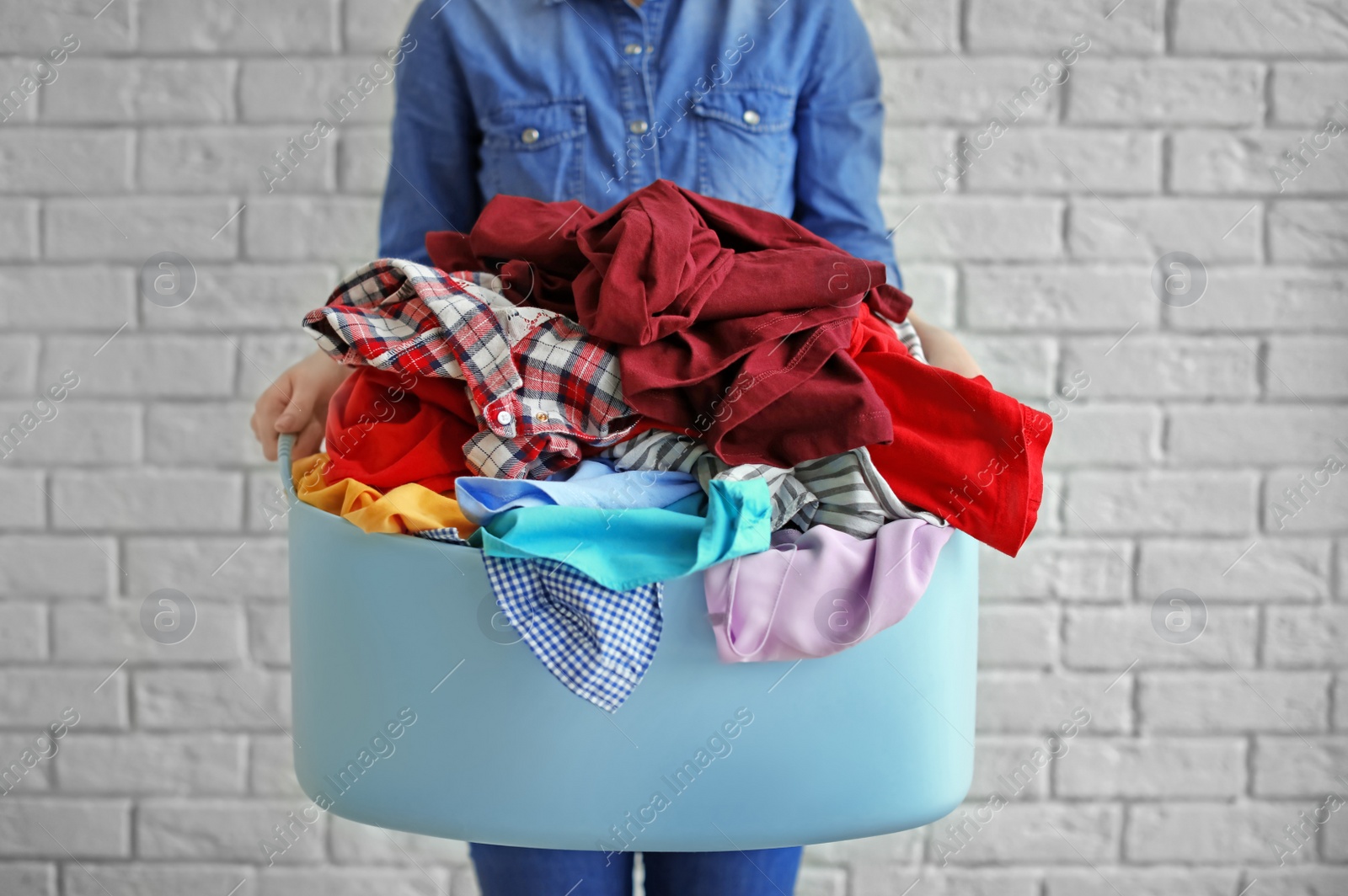 Photo of Woman holding laundry basket with dirty clothes on brick wall background