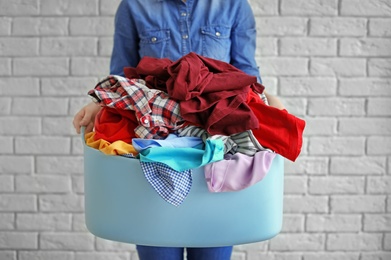 Photo of Woman holding laundry basket with dirty clothes on brick wall background