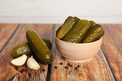 Photo of Bowl of pickled cucumbers, peppercorns and garlic on wooden table