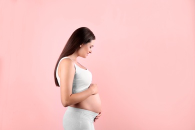 Photo of Beautiful pregnant woman holding hands on belly against color background. Space for text