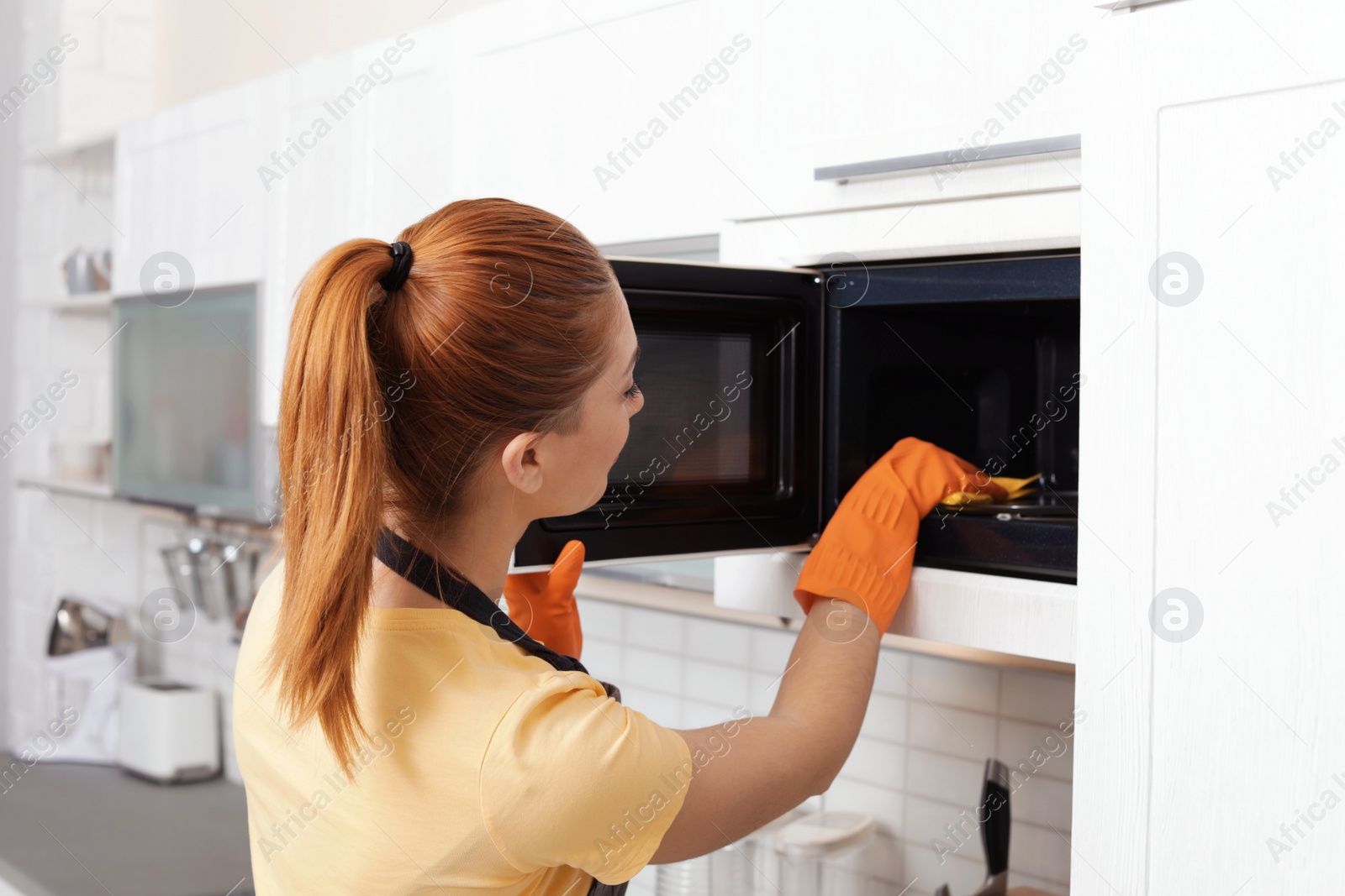 Photo of Woman cleaning microwave oven with rag in kitchen