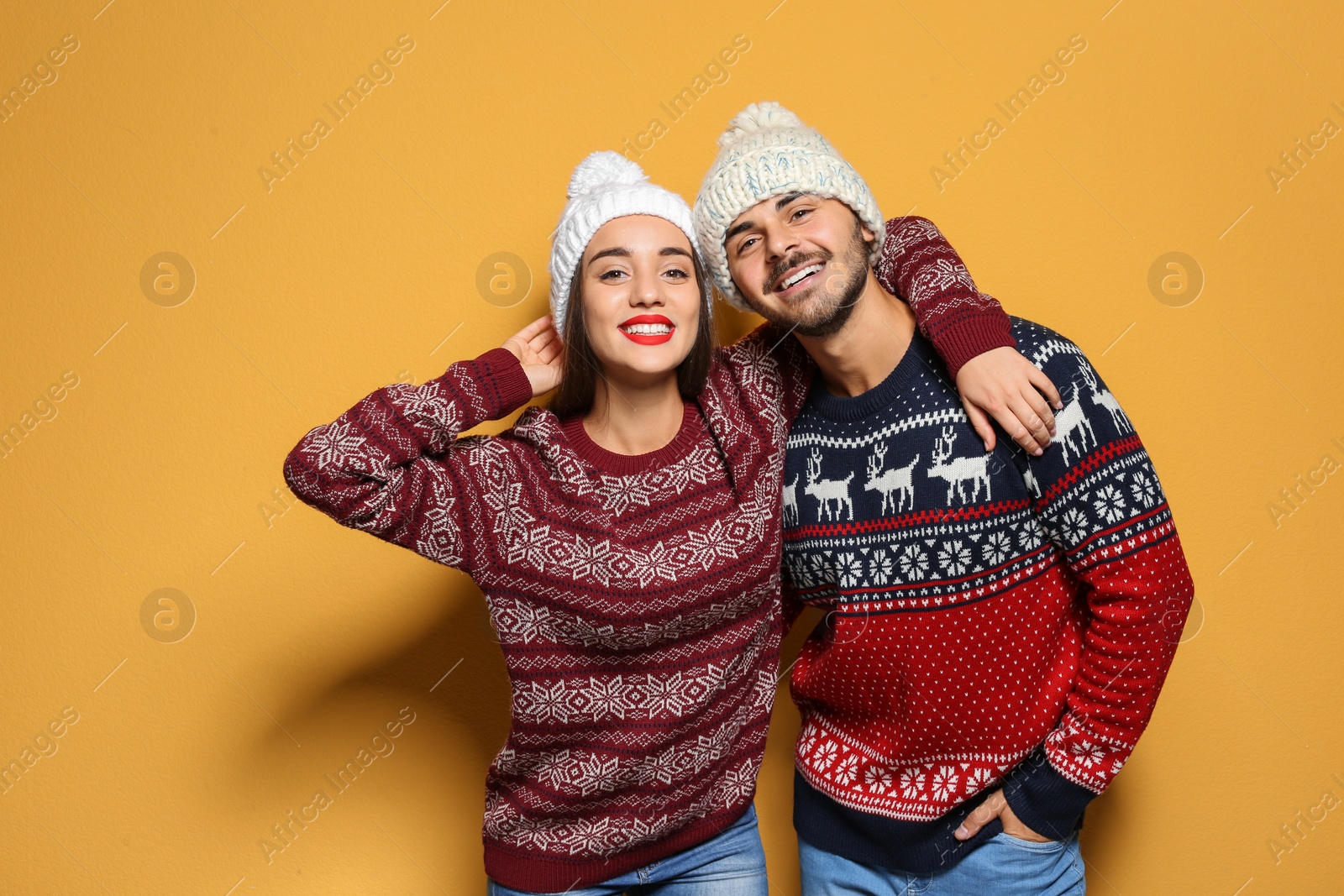 Photo of Young couple in warm sweaters and knitted hats on color background. Christmas celebration