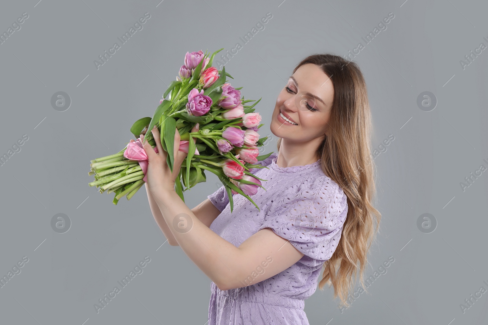 Photo of Happy young woman with bouquet of beautiful tulips on grey background