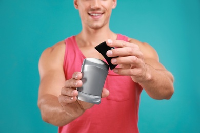 Young man with deodorant on light blue background, closeup