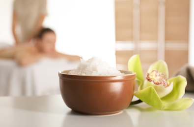 Photo of Bowl with sea salt and orchid flower on white table in spa salon