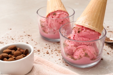 Photo of Delicious pink ice cream in wafer cones with almonds on light table, closeup