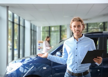 Salesman with clipboard near new car in modern auto dealership