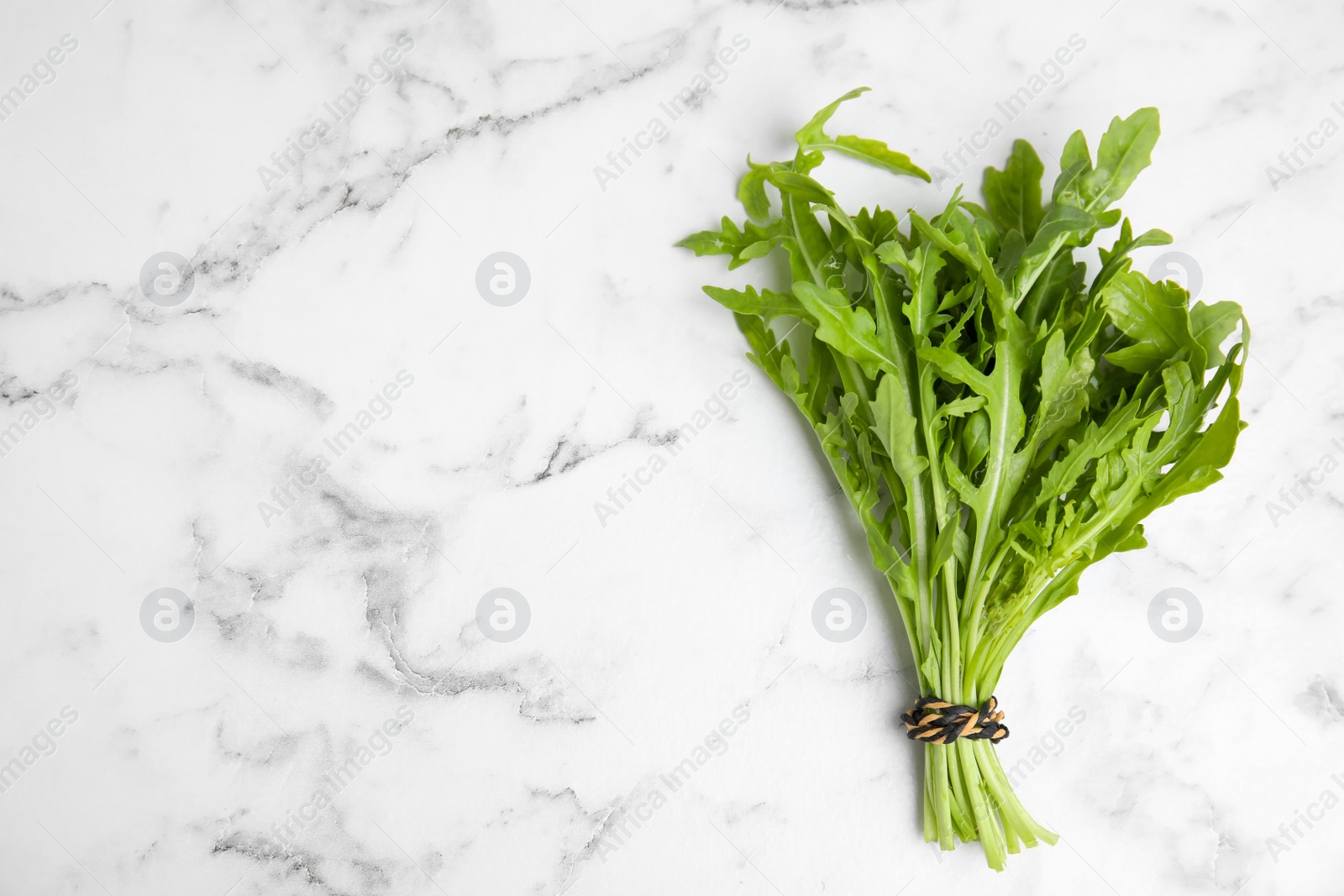 Photo of Fresh arugula on white marble table, top view. Space for text