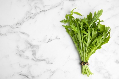 Photo of Fresh arugula on white marble table, top view. Space for text