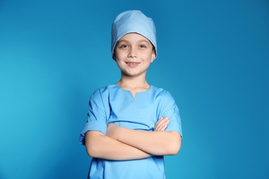 Cute little child in doctor uniform on color background