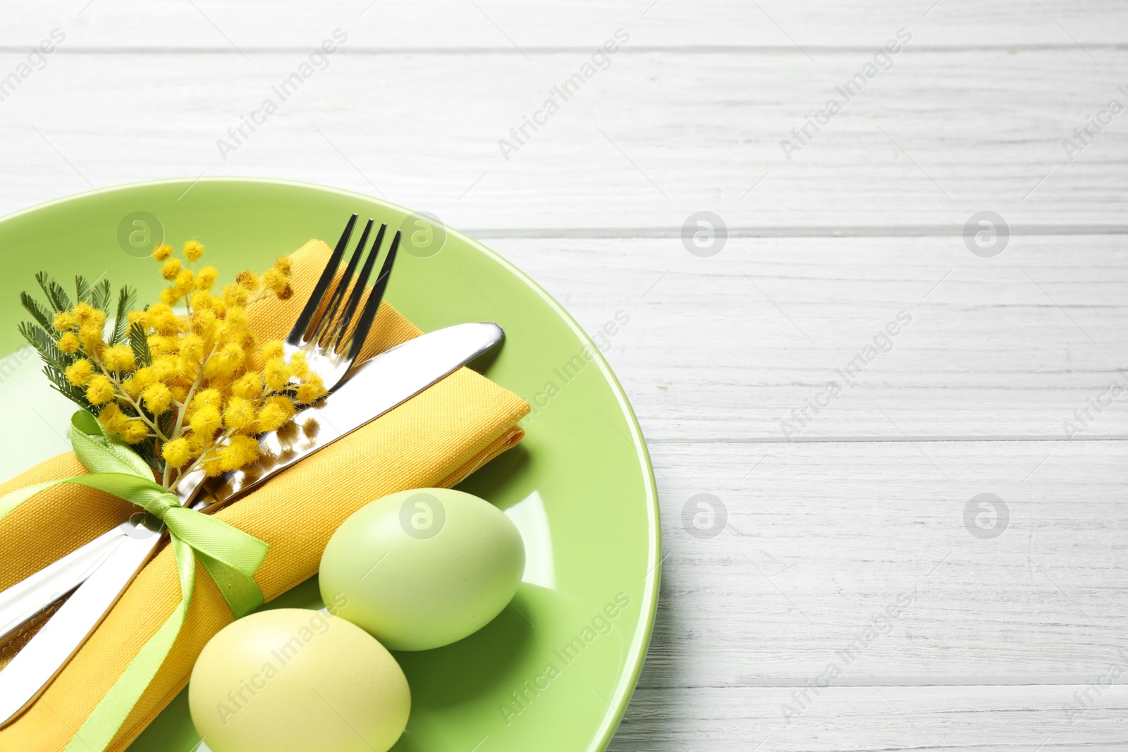 Photo of Festive Easter table setting with eggs and floral decor on white wooden background, above view. Space for text