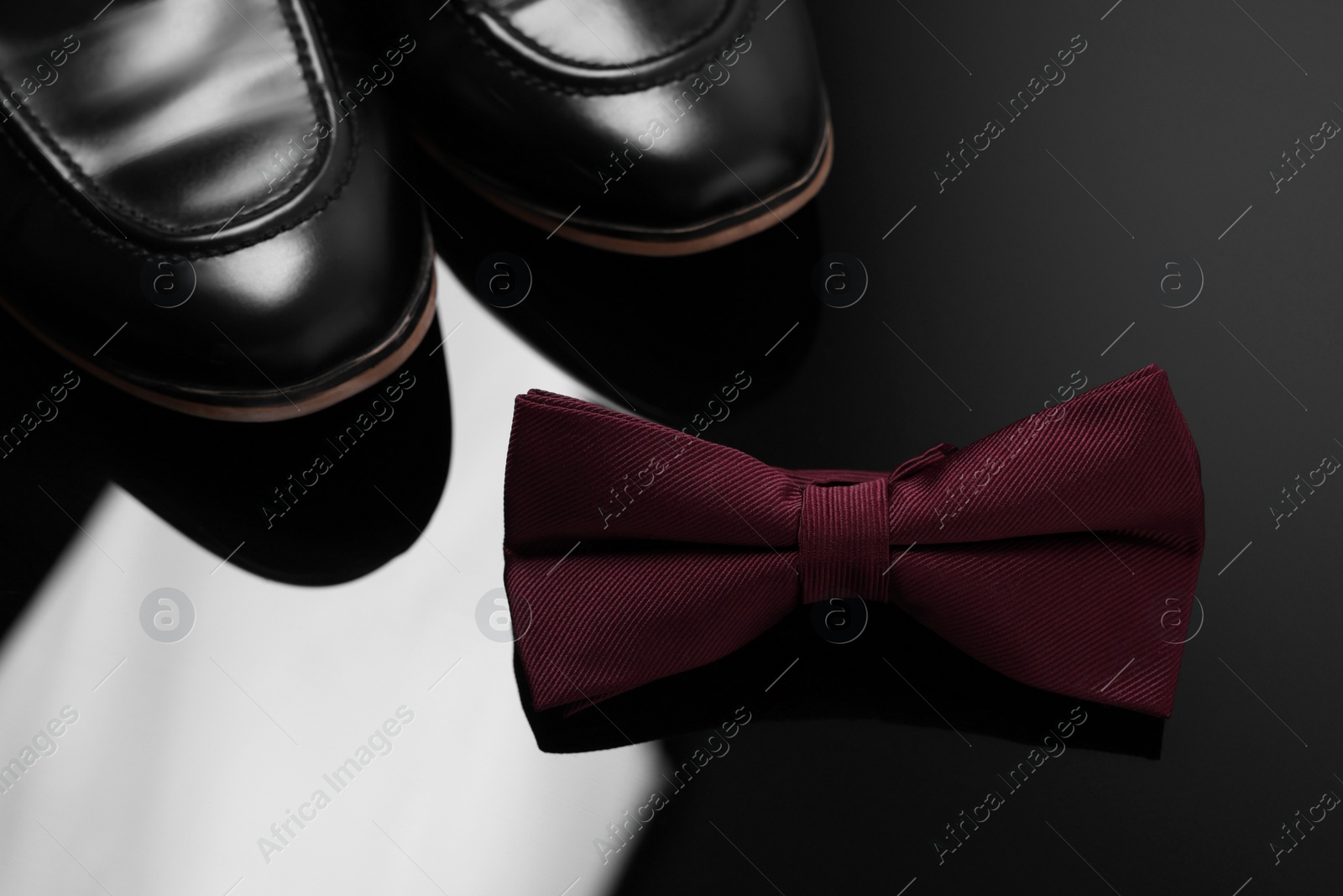 Photo of Stylish burgundy bow tie and shoes on black mirror surface