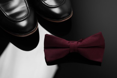 Stylish burgundy bow tie and shoes on black mirror surface