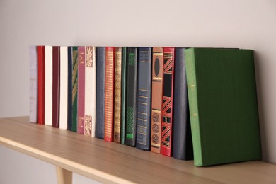 Photo of Wooden shelf with different books on light wall