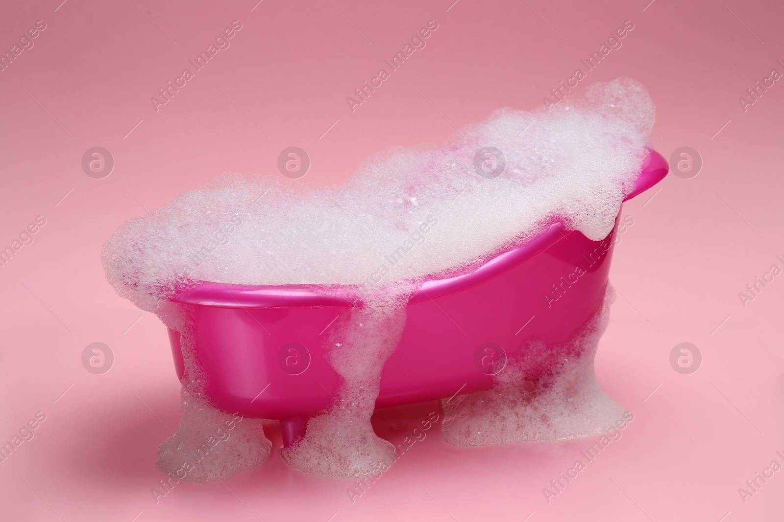 Photo of Toy bathtub overflowing with foam on pink background