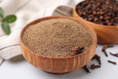 Aromatic clove powder and dried buds in bowls on white table, closeup