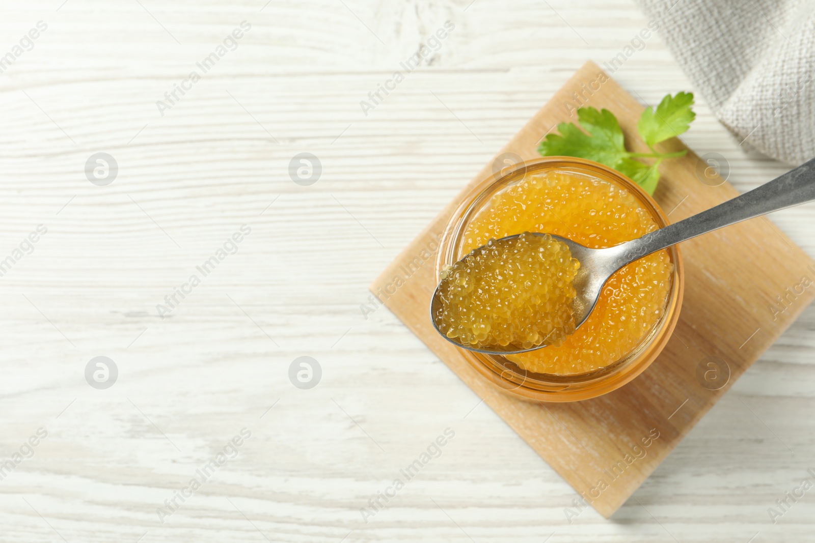 Photo of Fresh pike caviar in glass jar, parsley and spoon on white wooden table, top view. Space for text