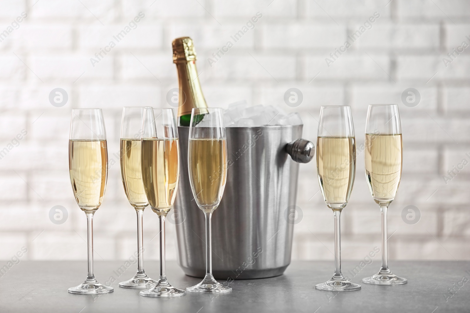 Photo of Glasses with champagne and bottle in bucket on table against brick wall