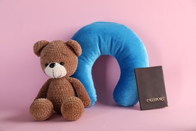 Photo of Light blue travel pillow, toy bear and passport on pink background