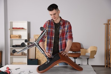 Young handyman repairing desk chair in room