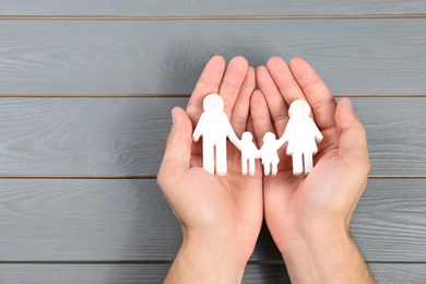 Photo of Young man holding family figure in his hands against grey wooden background, top view. Space for text