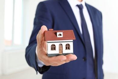Real estate agent holding house model on blurred background, closeup