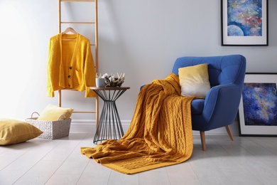 Photo of Soft knitted blanket on armchair in room. Home interior