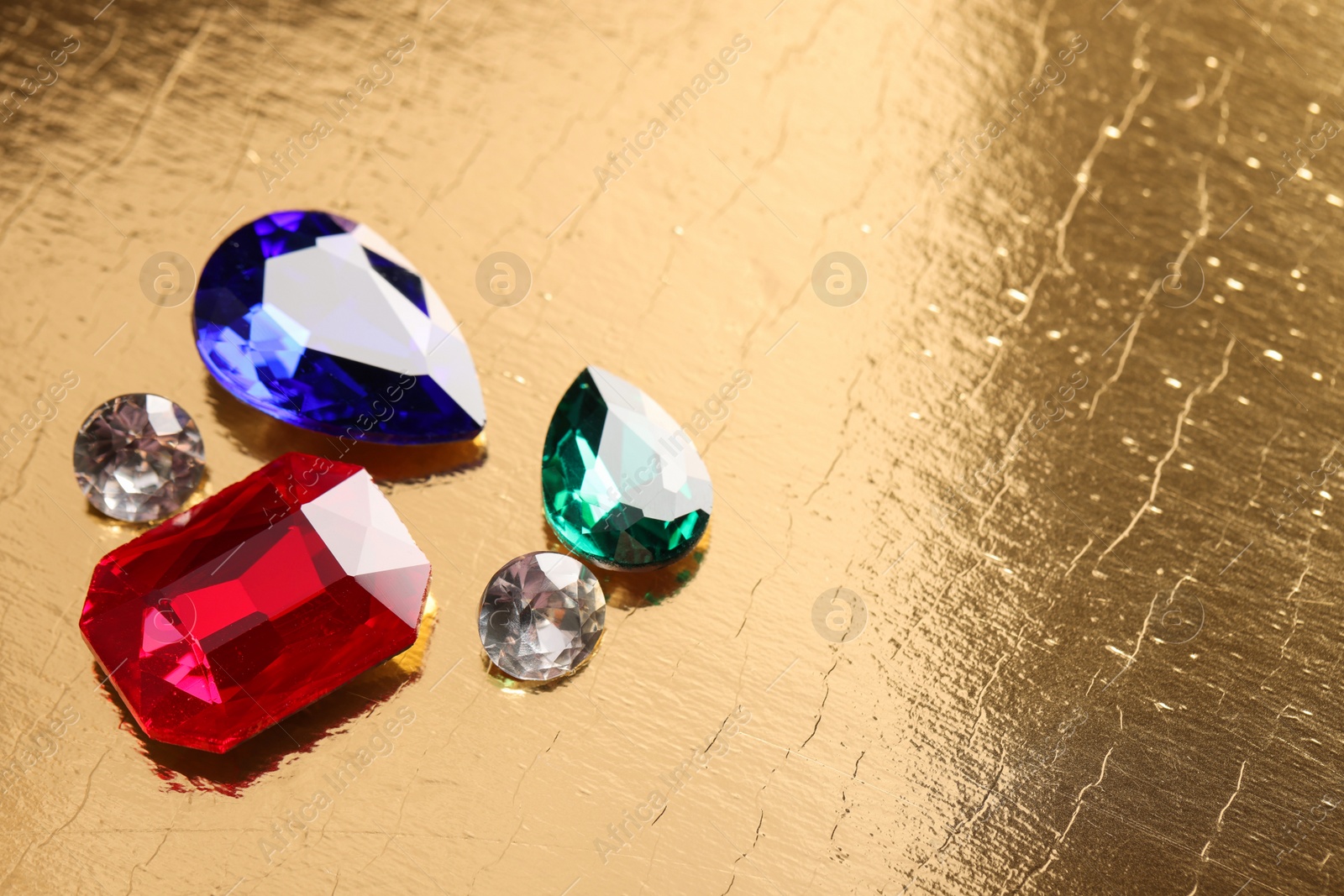 Photo of Different beautiful gemstones for jewelry on golden background, above view. Space for text