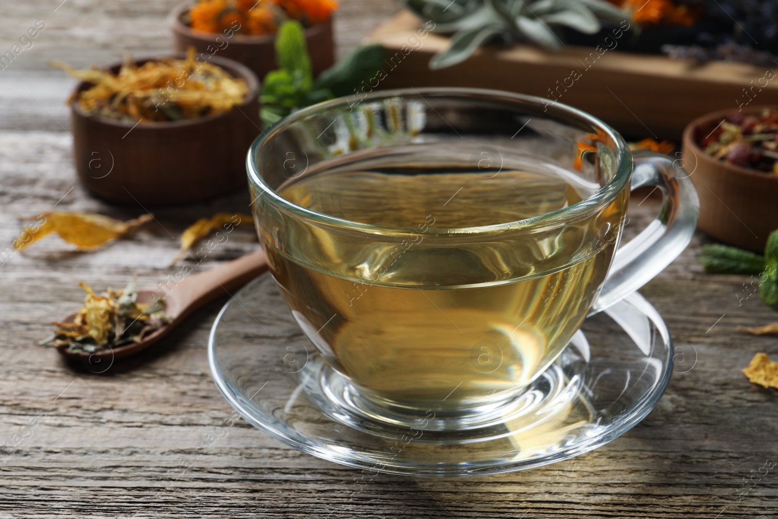 Photo of Glass cup of aromatic freshly brewed tea near different dry herbs on wooden table