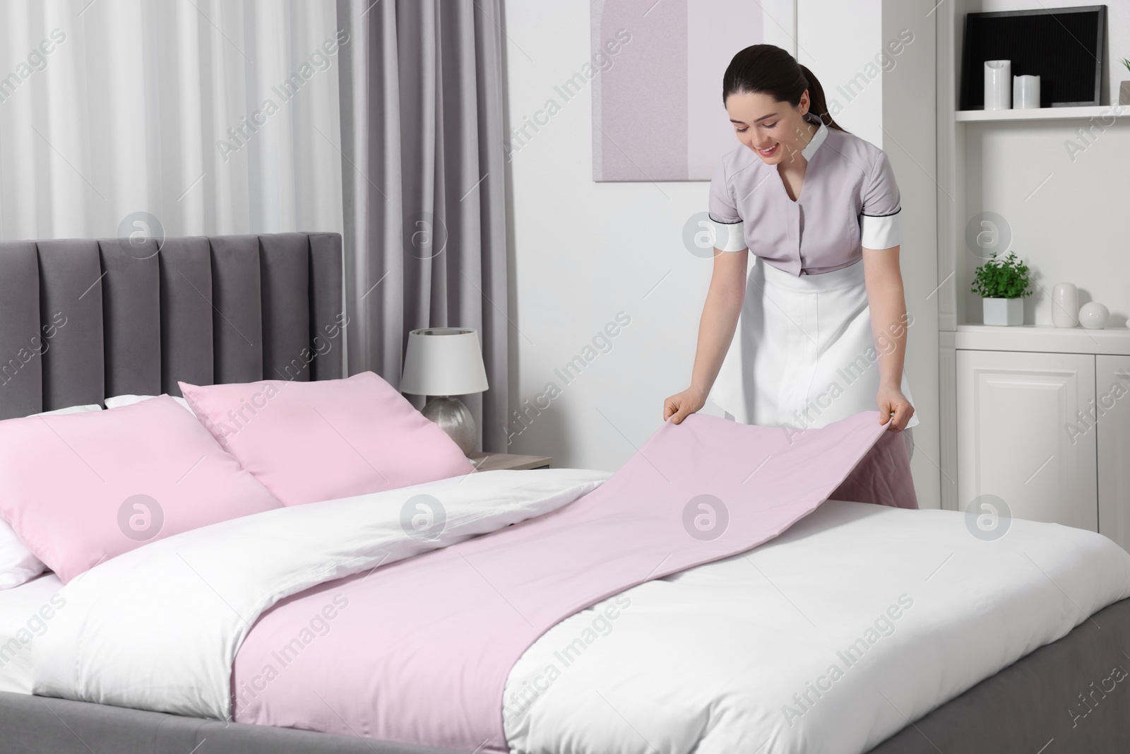 Photo of Young maid making bed in hotel room