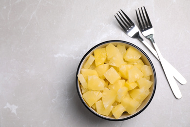 Photo of Tasty canned pineapple pieces and forks on light grey marble table, flat lay. Space for text