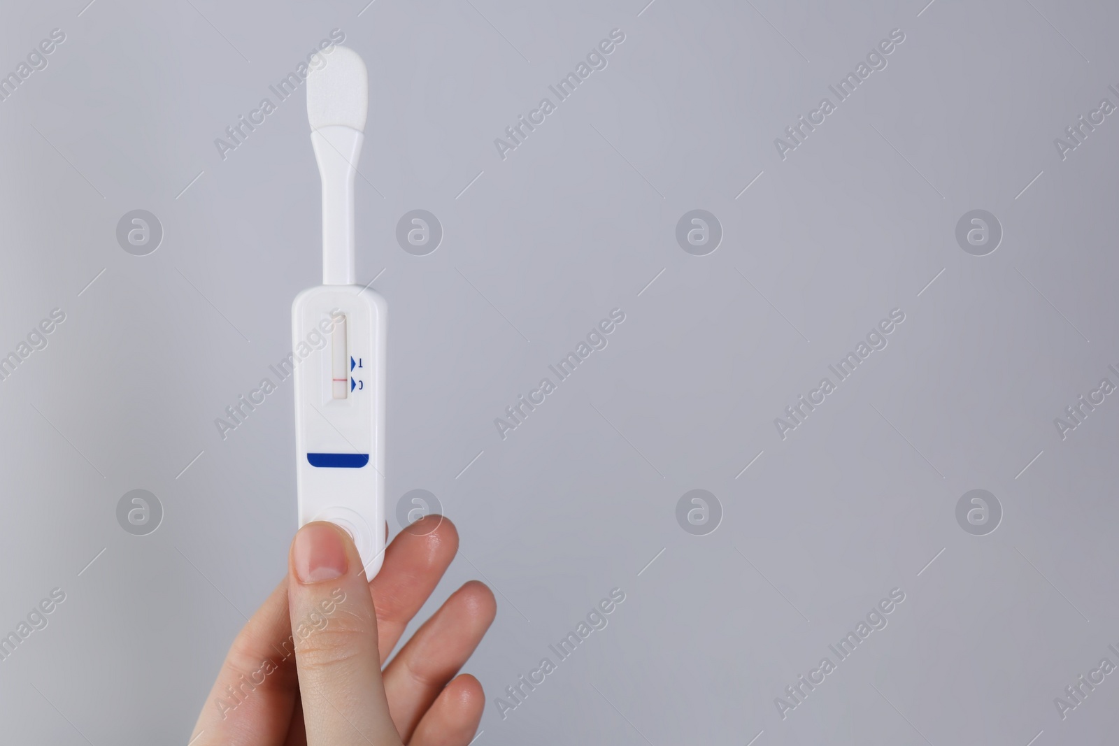 Photo of Woman holding disposable express test on light grey background, closeup. Space for text