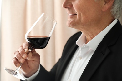 Senior man with glass of wine indoors, closeup